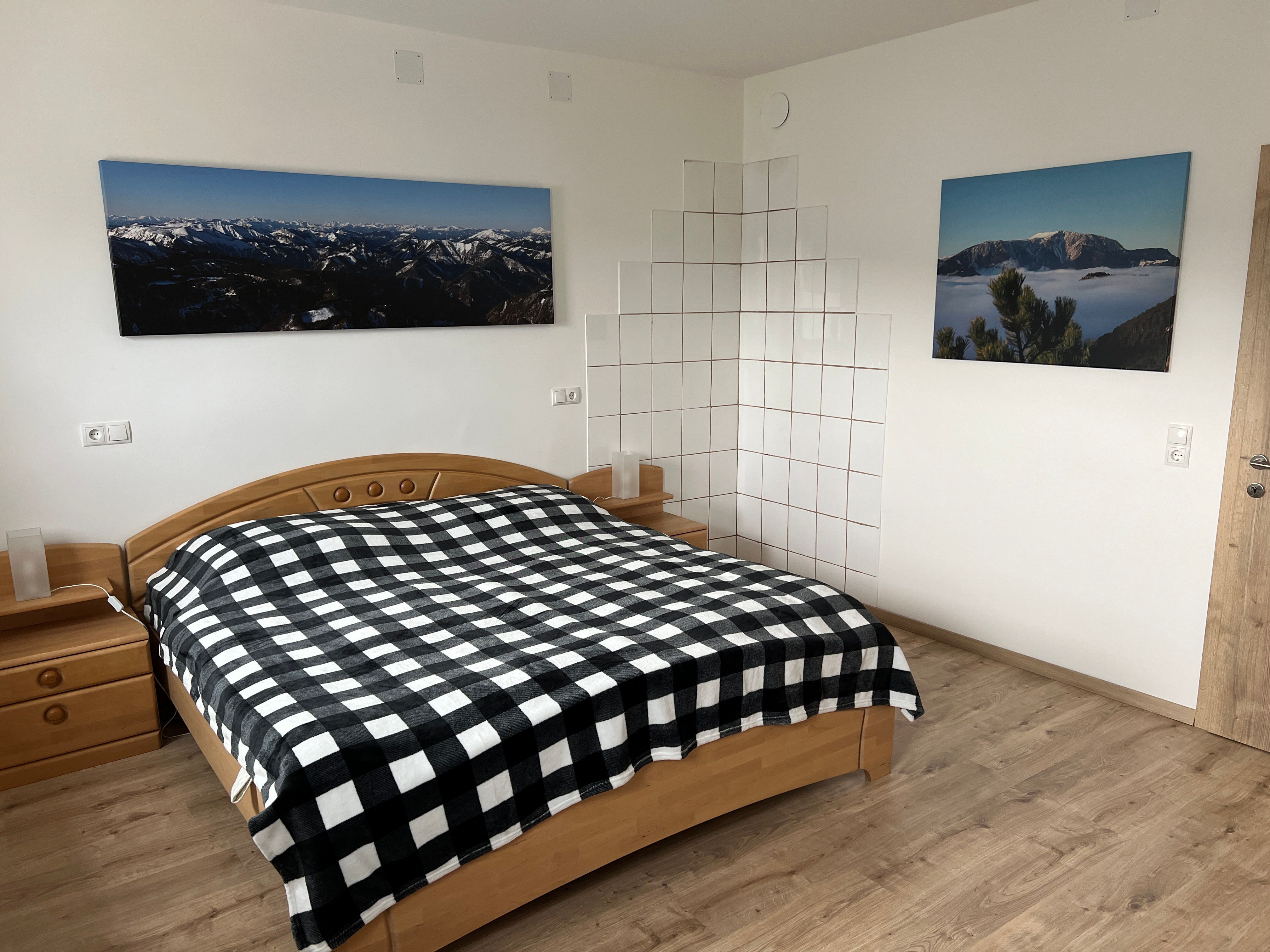 Schlafzimmer mit Doppelbett, kariertem Bettüberwurf, Holzmöbeln und Berglandschaftsbildern an der Wand.