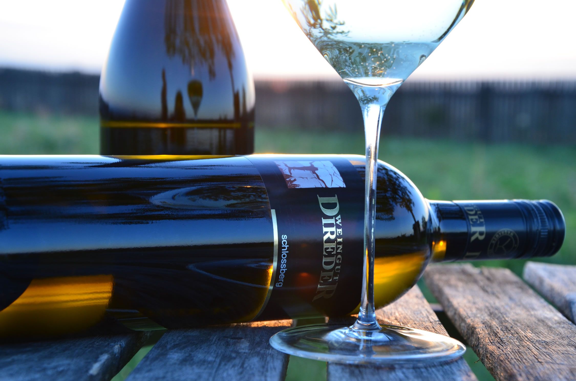 Weinflasche und Glas auf Holztisch im Freien.