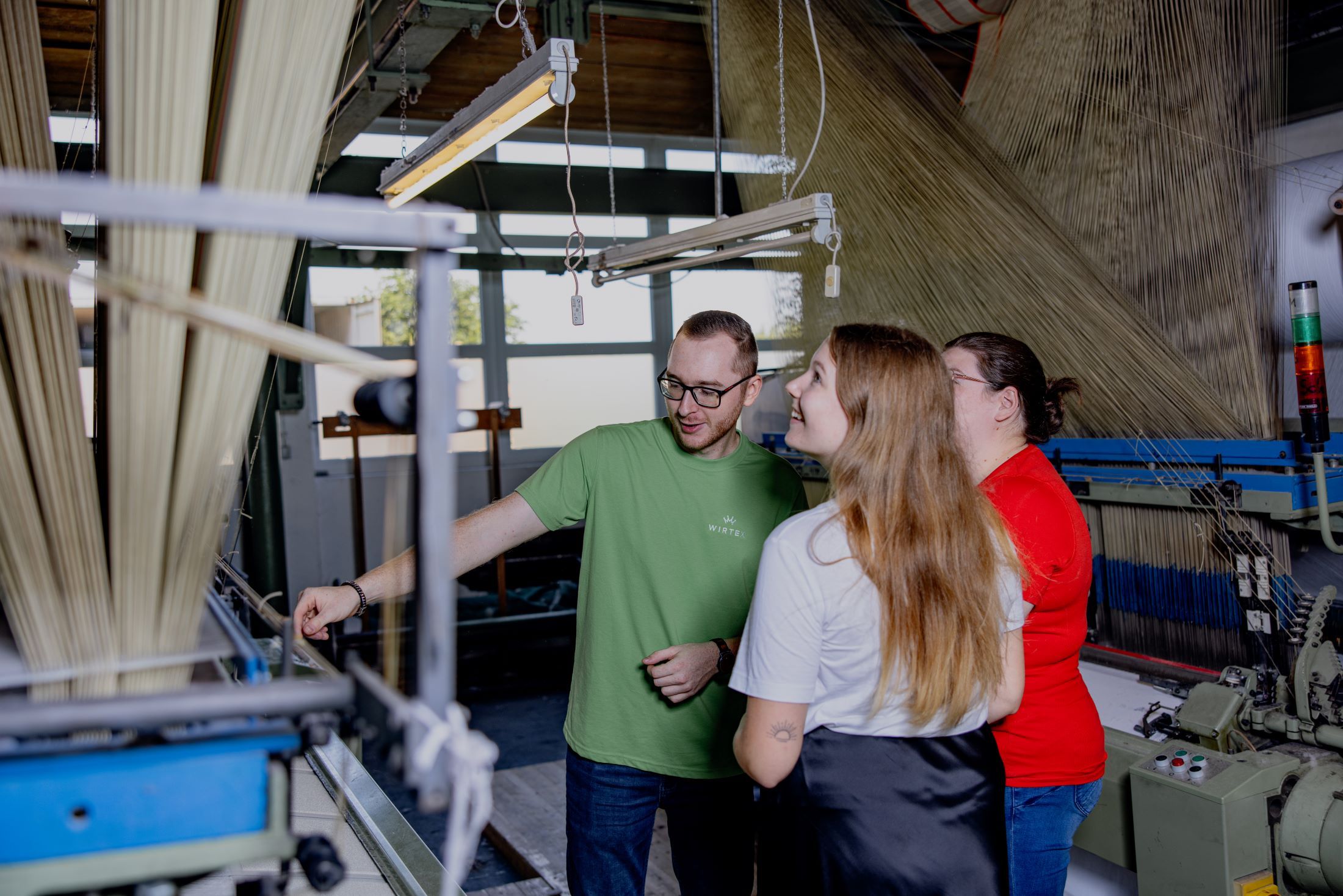 Drei Personen in einer Textilfabrik betrachten eine Maschine.