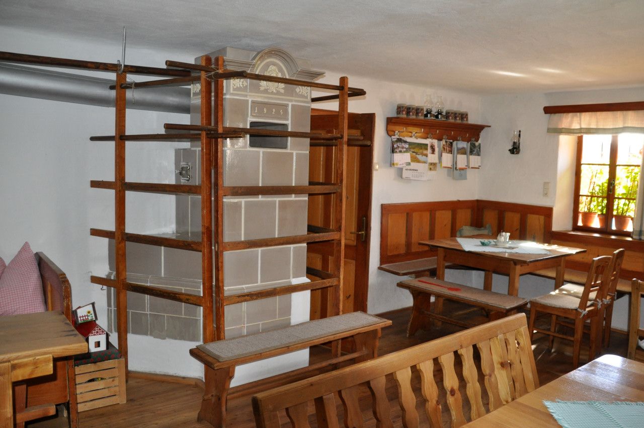 Innenansicht eines traditionellen Bauernhauses mit Kachelofen und Holzmöbeln.