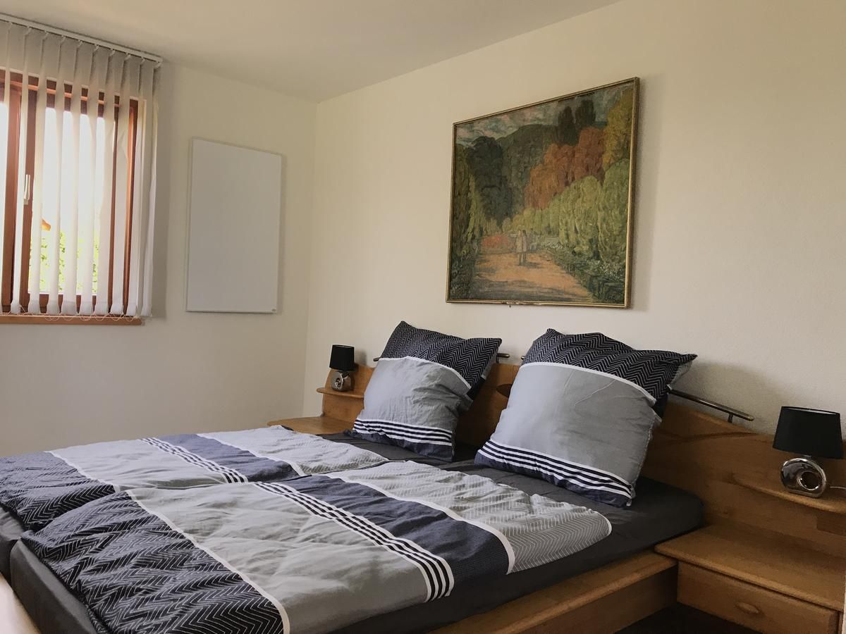 Ein gemütliches Schlafzimmer mit einem Doppelbett, grauer Bettwäsche, einem Gemälde an der Wand und einem Fenster mit Jalousien.