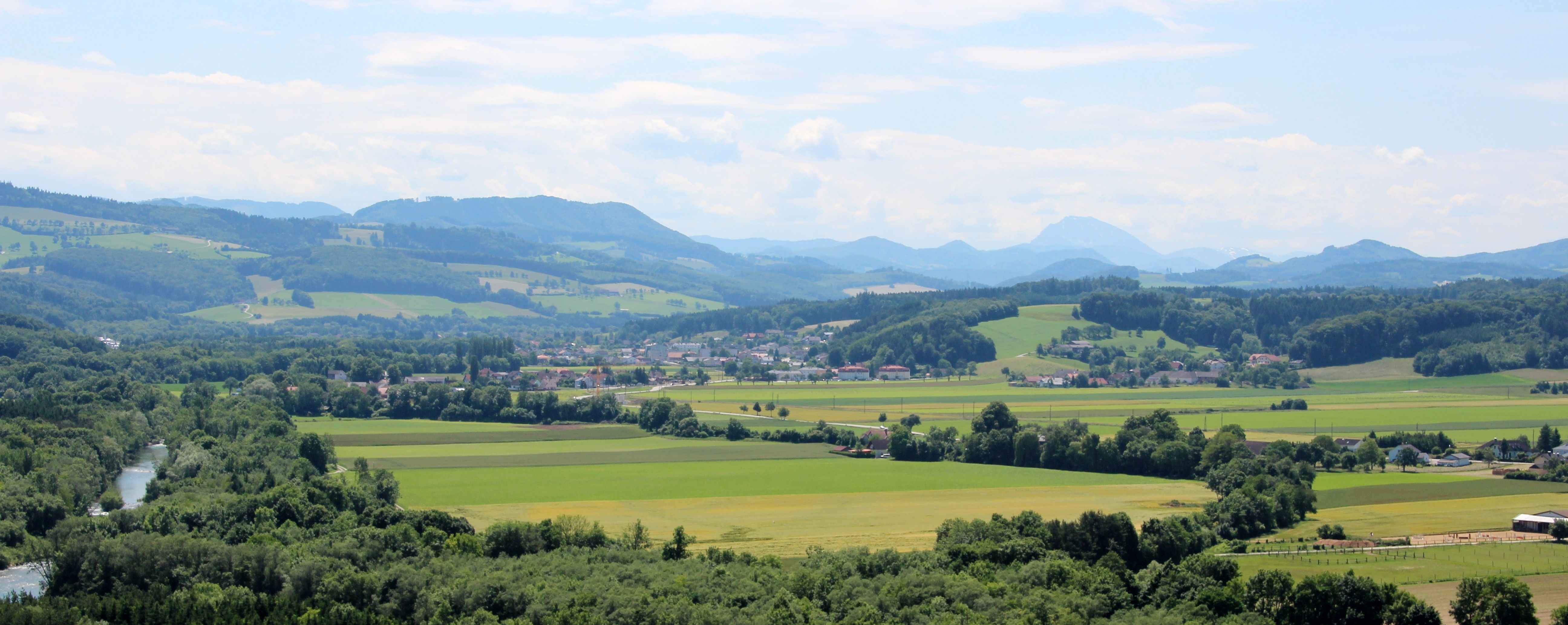 Panorama einer grünen Landschaft mit Hügeln, Feldern und einem Fluss.