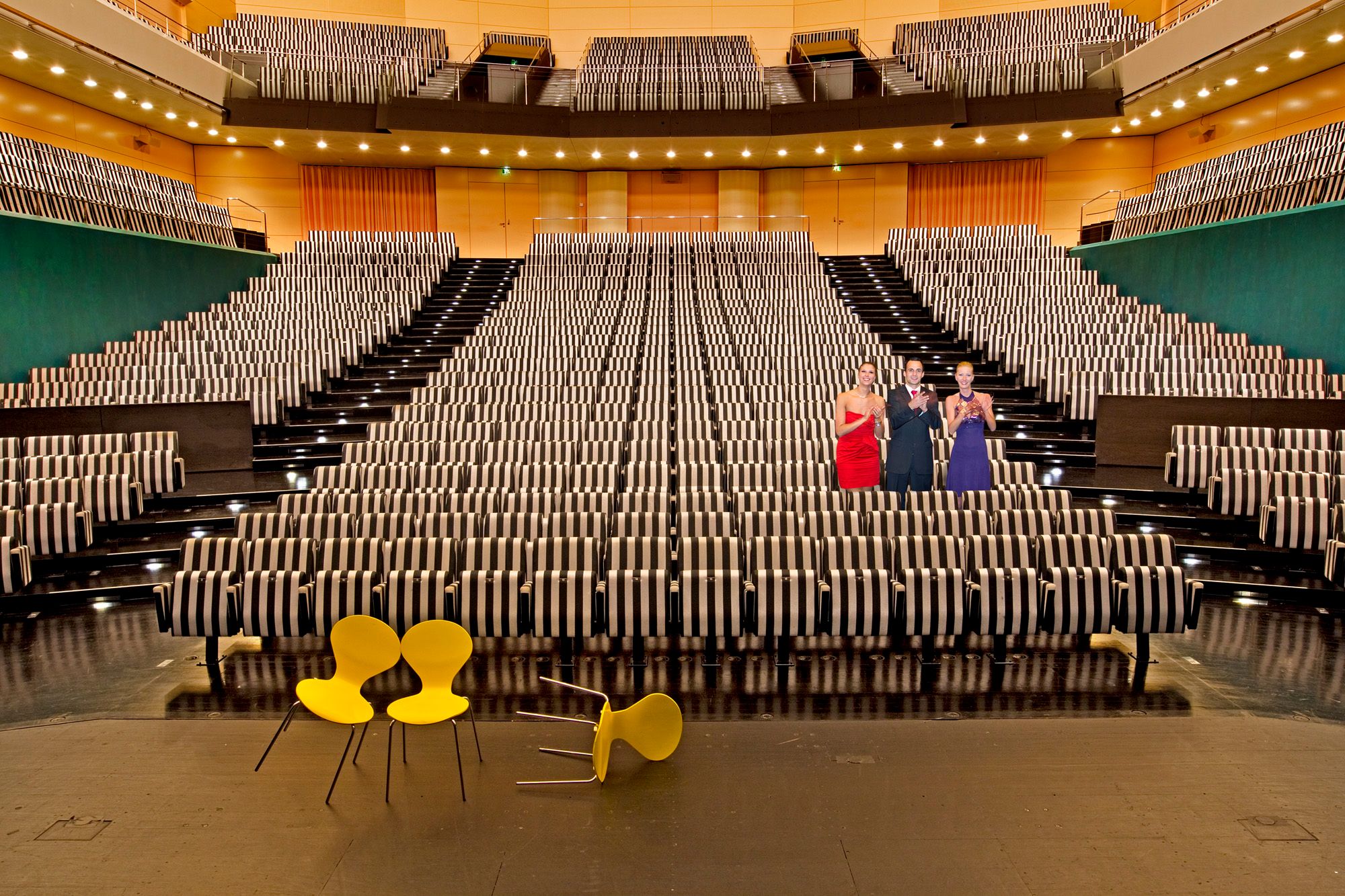 Das Innere des großen Saales im Festspielhaus St. Pölten mit Sesselreihen mit gestreiften Sesseln, im Vordergrund drei gelbe Sessel, von denen einer umgefallen ist