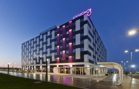Außenansicht des Moxy Vienna Airport Hotels bei Dämmerung mit beleuchtetem Schriftzug.