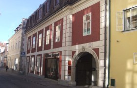 Historisches Gebäude mit roter Fassade und Torbogen in einer Straße.