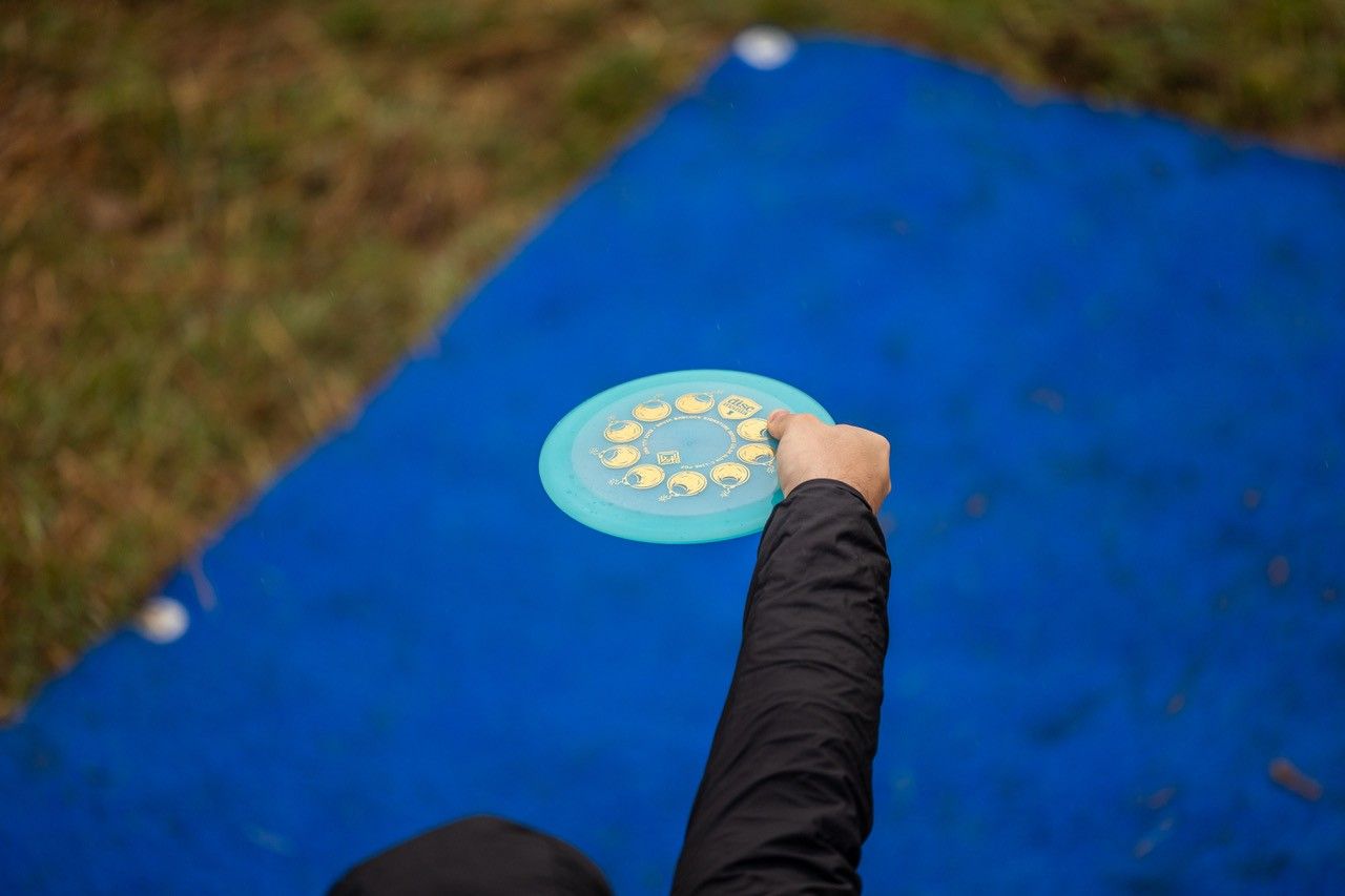 Person hält eine Discgolf-Scheibe über einer blauen Matte, die Hand zum Wurf ausgestreckt