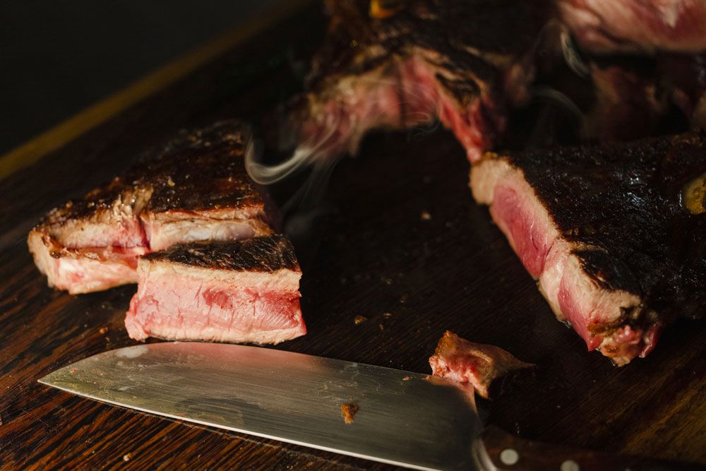 Nahaufnahme von geschnittenem Steak auf einem Holzbrett mit einem Messer daneben.