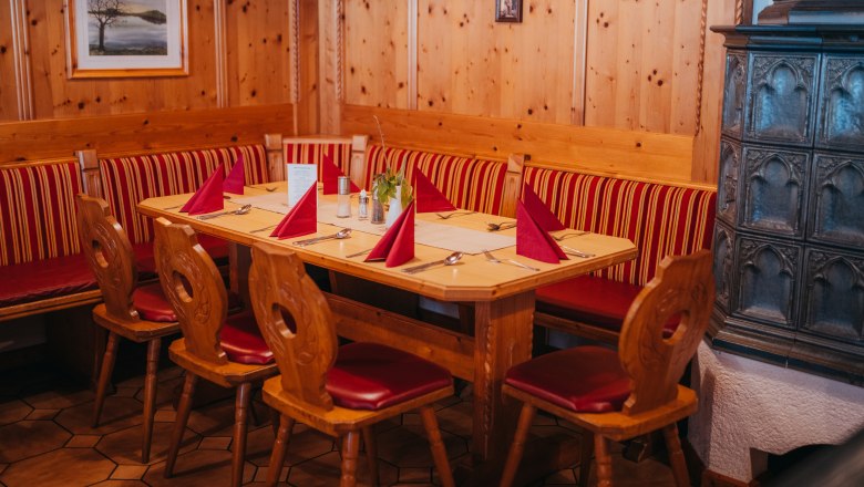 Gem&uuml;tliche Stube mit Holzm&ouml;beln, rotem Polster und Kachelofen.