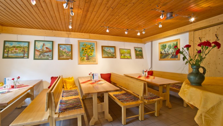 Innenansicht eines Heurigenlokals mit Holzm&ouml;beln und Gem&auml;lden an der Wand.