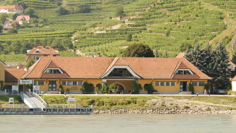Gelbes Gebäude mit rotem Dach vor Weinbergen in Spitz an der Donau.