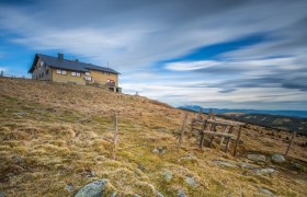 Berghütte auf einem Hügel mit bewölktem Himmel im Hintergrund.