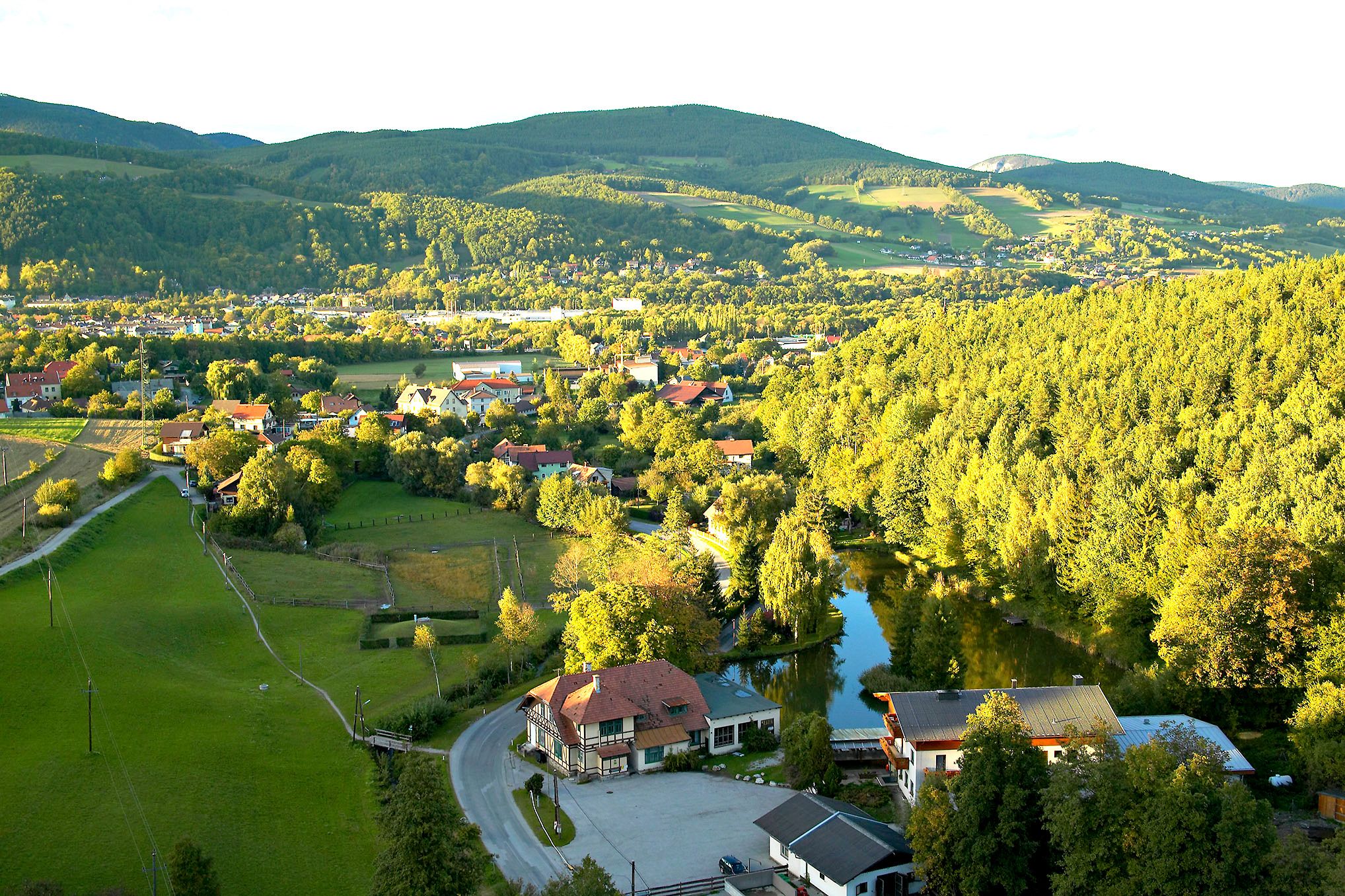 Landschaftsansicht von Enzenreith mit Häusern, Wäldern und Hügeln im Hintergrund.
