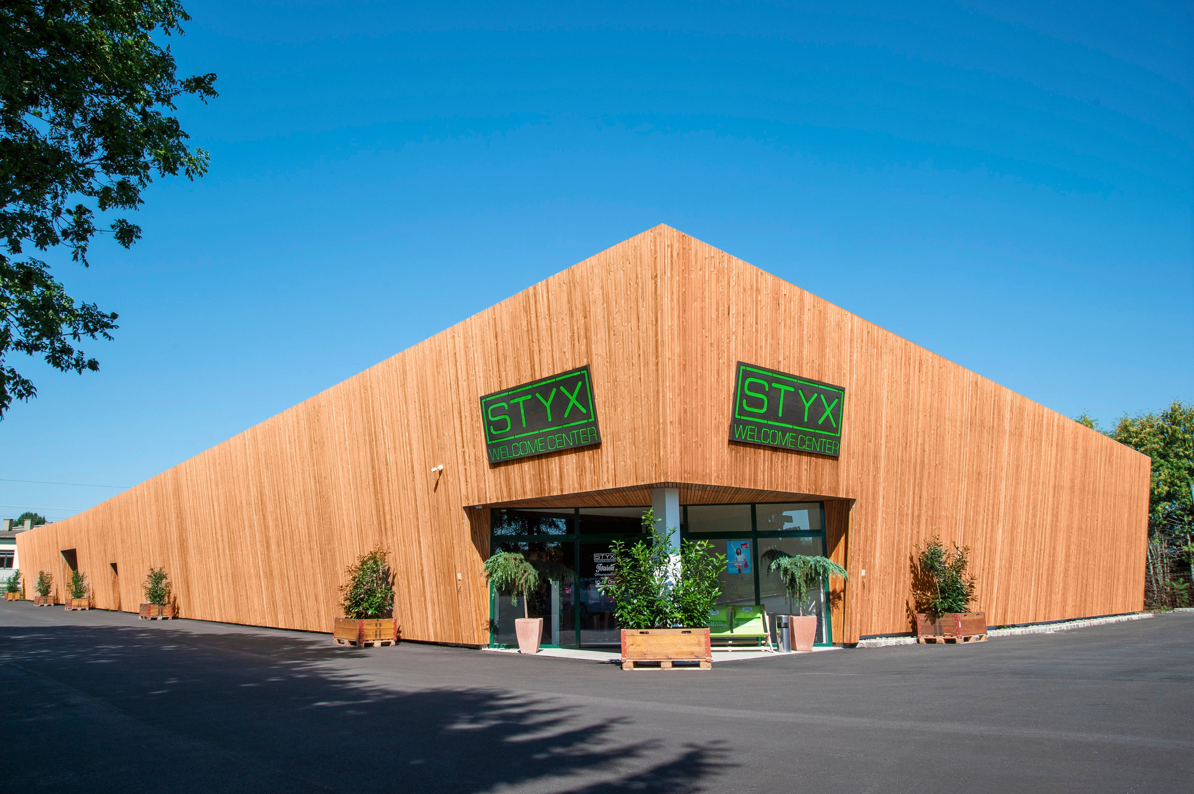 Ein modernes Gebäude mit Holzverkleidung und grünen Schildern mit der Aufschrift 'STYX Welcome Center'.
