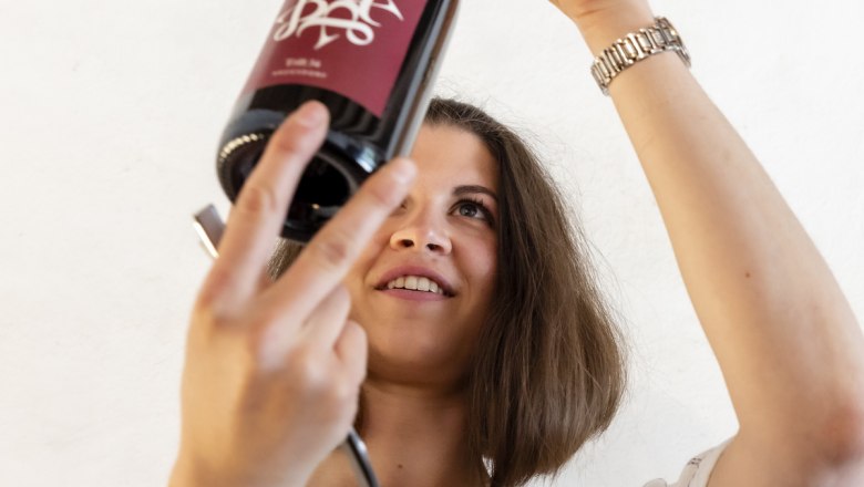 Frau inspiziert eine Weinflasche gegen das Licht.