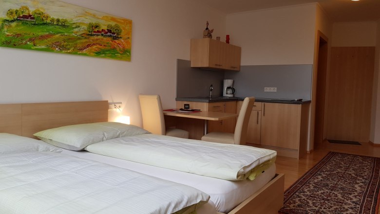 Zimmer, © BIO-Weingut Poys Ein modernes Zimmer mit zwei Betten, einem Schreibtisch, einer kleinen Küchenzeile und einem bunten Gemälde an der Wand.