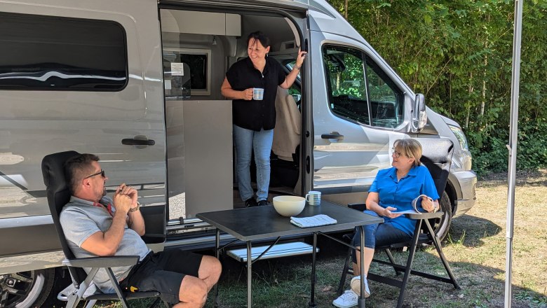 Camping Harrachpark, © Donau Niederösterreich, Wagner Drei Personen entspannen vor einem Wohnmobil im Freien.