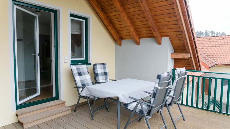 Dachterrasse mit Tisch und Stühlen unter einem Holzdach.