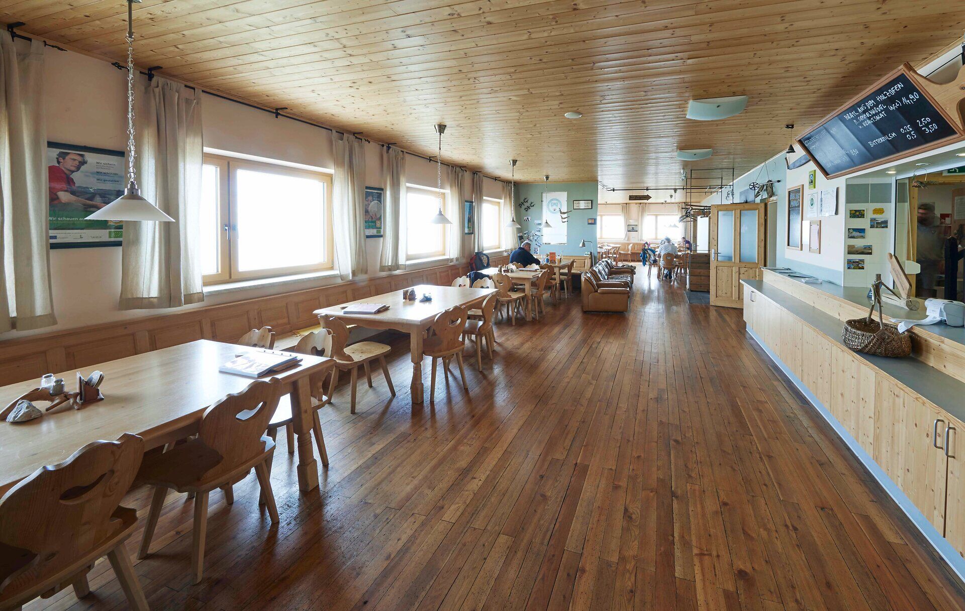 Heller Gastraum mit Holztischen, großen Fenstern und Bergblick.