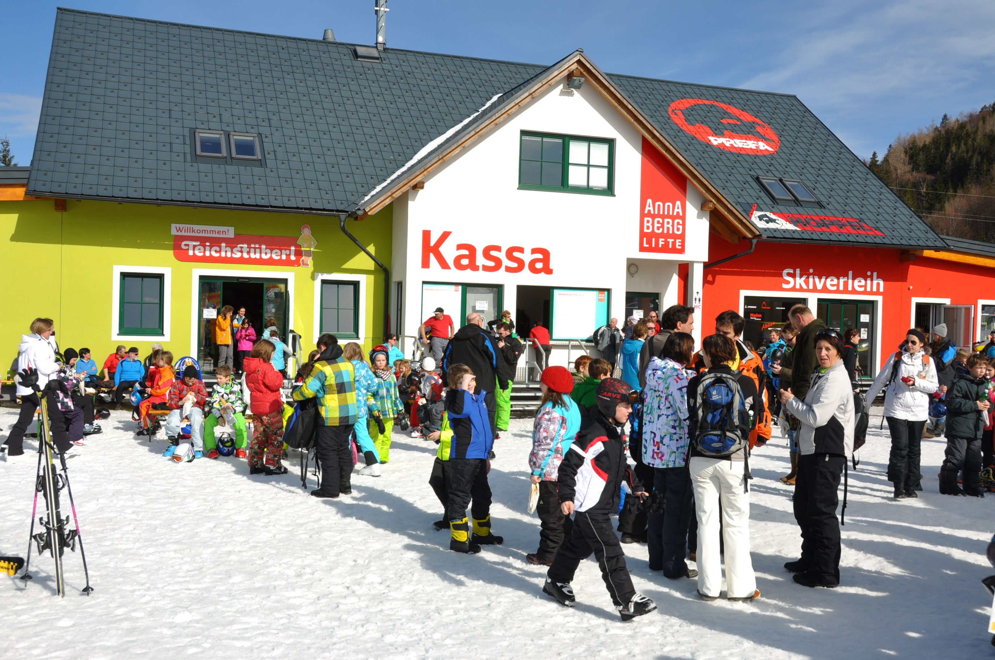 Menschenmenge vor einem Skigebäude mit Kassa, Skiverleih und Teichstüberl.