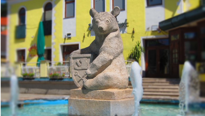 Steinbär-Skulptur mit Wappen in einem Brunnen vor einem gelben Gebäude.