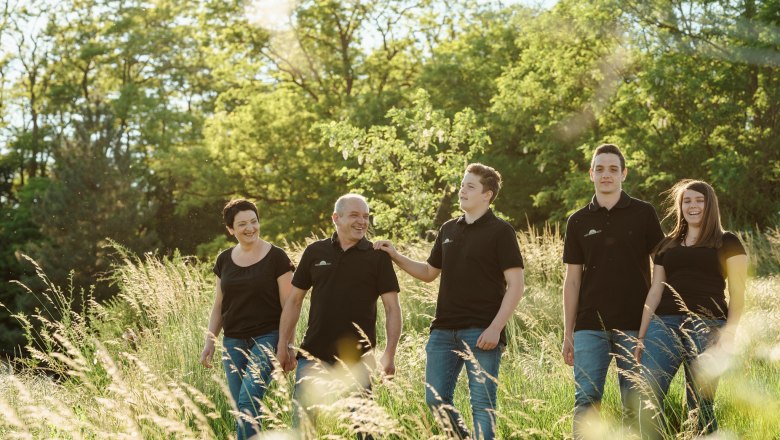 Eine Familie spaziert lächelnd durch eine grüne Wiese bei Sonnenschein.