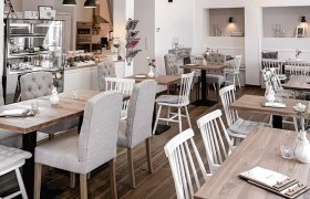 Innenansicht eines gemütlichen Cafés mit Holztischen und gepolsterten Stühlen.