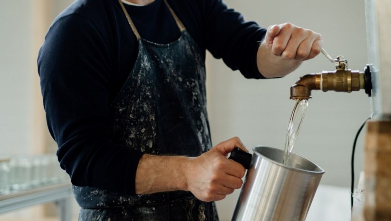 Person füllt Wasser aus einem Hahn in einen Metallbehälter.