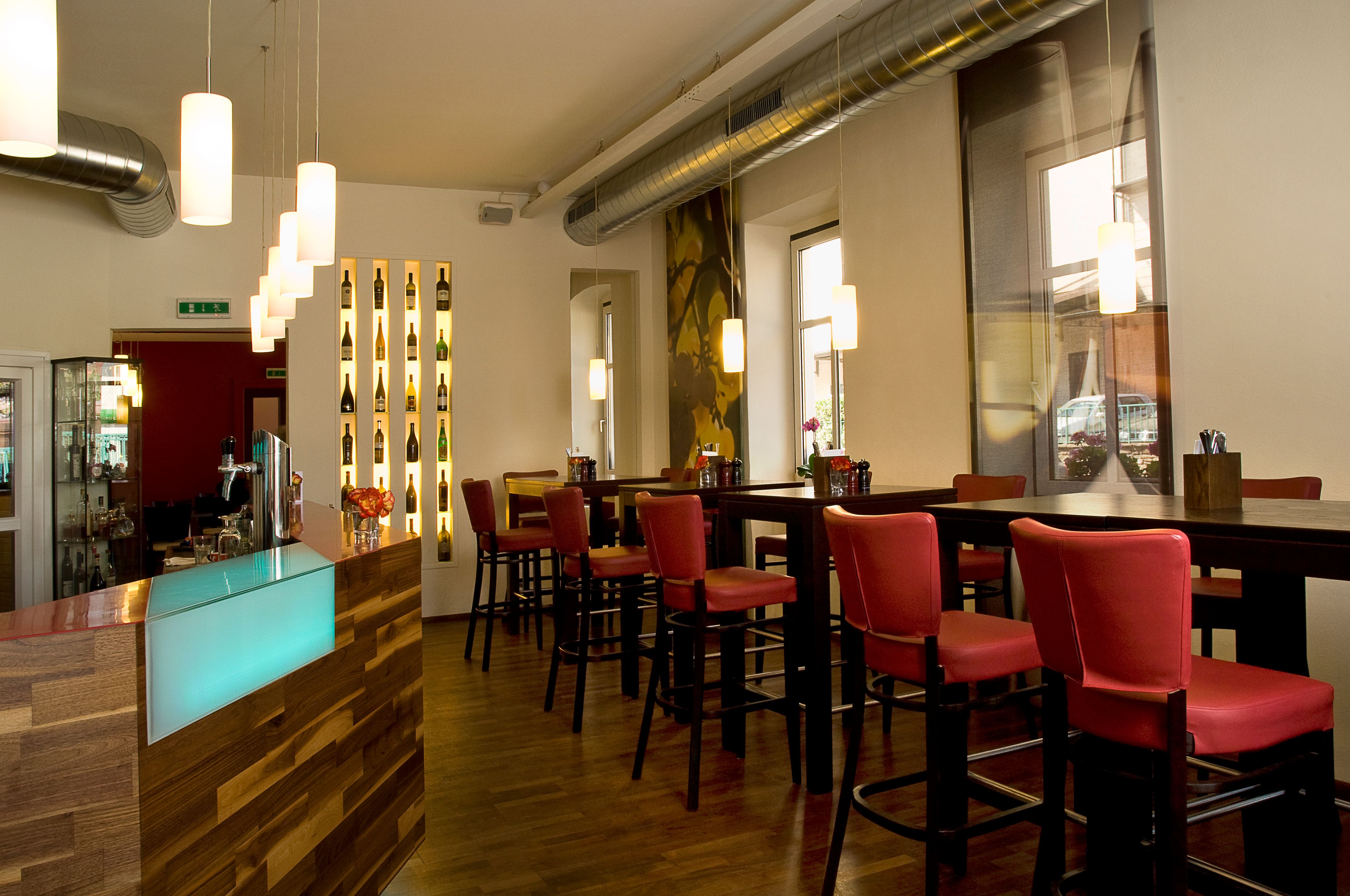 Innenansicht eines modernen Restaurants mit roten Stühlen und hölzernem Tresen.