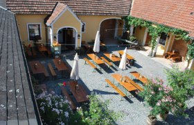 Innenhof einer Buschenschank mit Holztischen und Sonnenschirmen.