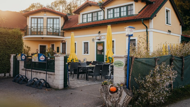 Gasthaus mit Terrasse, gelben Sonnenschirmen und Blumendekor.