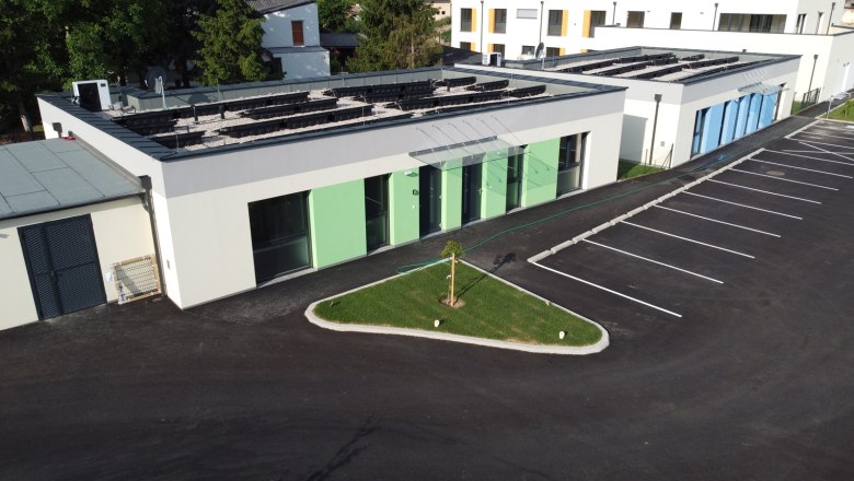 Au&szlig;enansicht von modernen Ferienbungalows mit gr&uuml;nem und blauem Anstrich, Parkplatz und kleinem Rasenbereich.