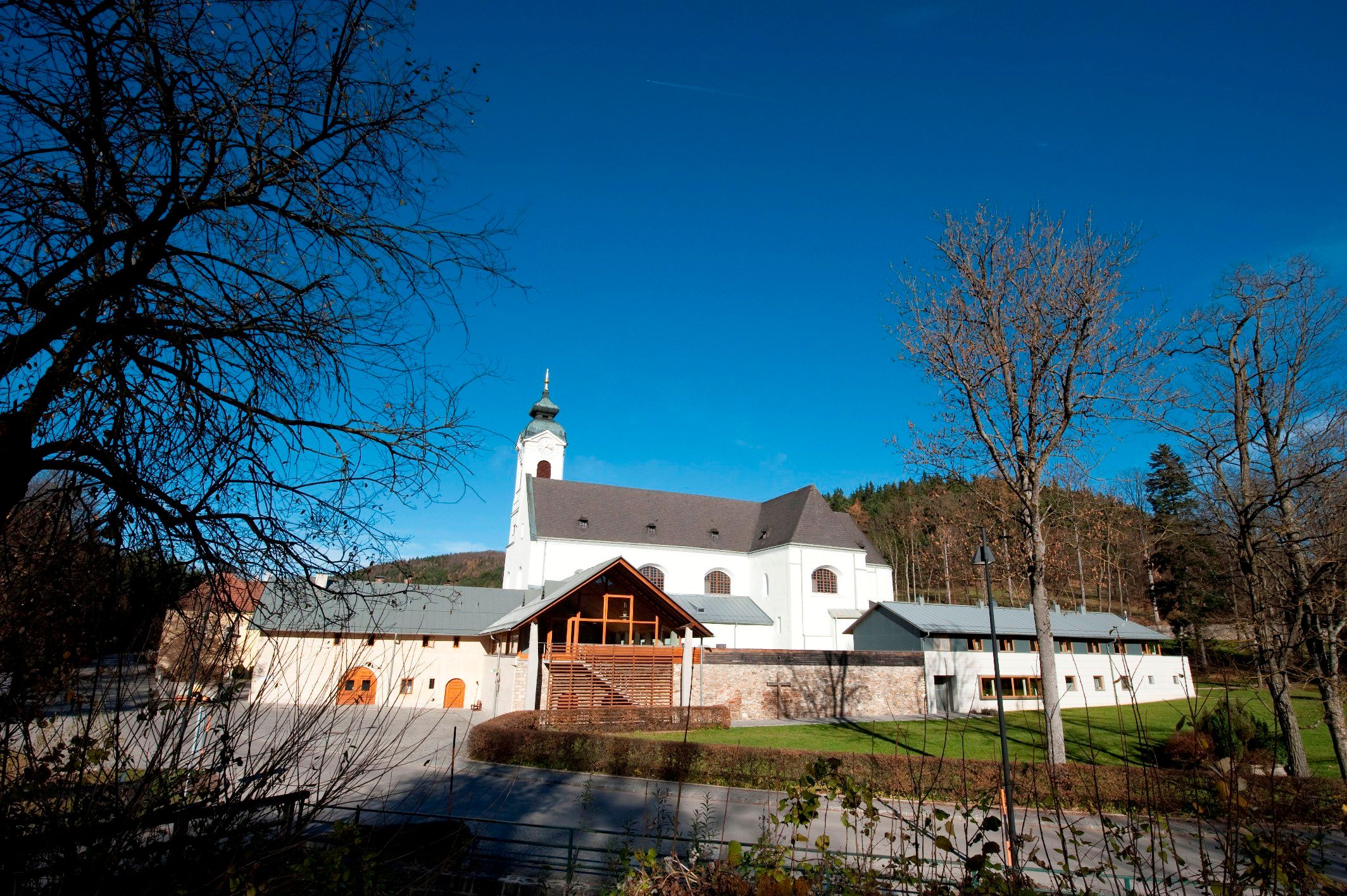 Wallfahrtskirche Klein-Mariazell mit blauem Himmel und Bäumen im Vordergrund.