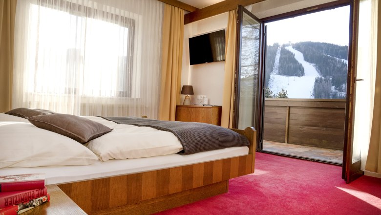 Hotelzimmer mit offenem Balkon und Blick auf eine schneebedeckte Skipiste.