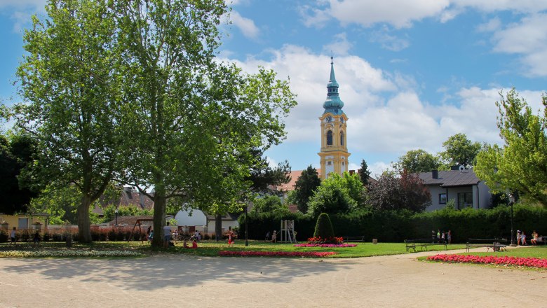 Ein Park mit Blumenbeeten, B&auml;umen und einem Kirchturm im Hintergrund.