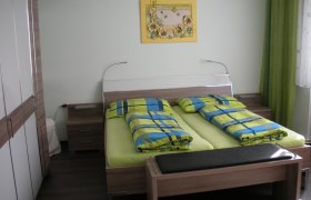 G&auml;stezimmer mit Doppelbett, bunter Bettw&auml;sche und Wandbild.