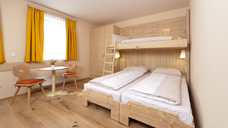 Gem&uuml;tliches G&auml;stezimmer mit Etagenbett, Holzm&ouml;beln und gelben Vorh&auml;ngen.