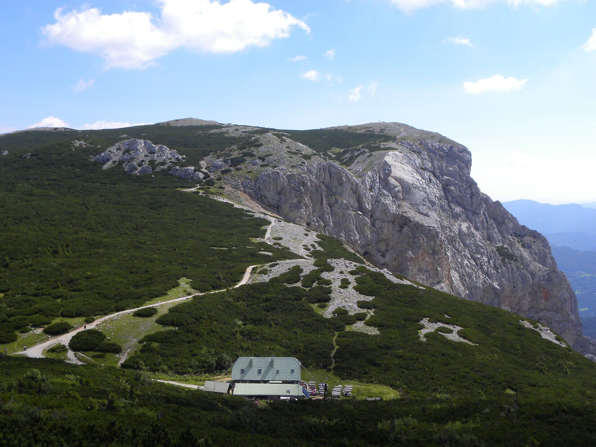 Berglandschaft auf der Rax mit markanten Felsformationen, Wanderwegen und einer Schutzhütte unter blauem Himmel.