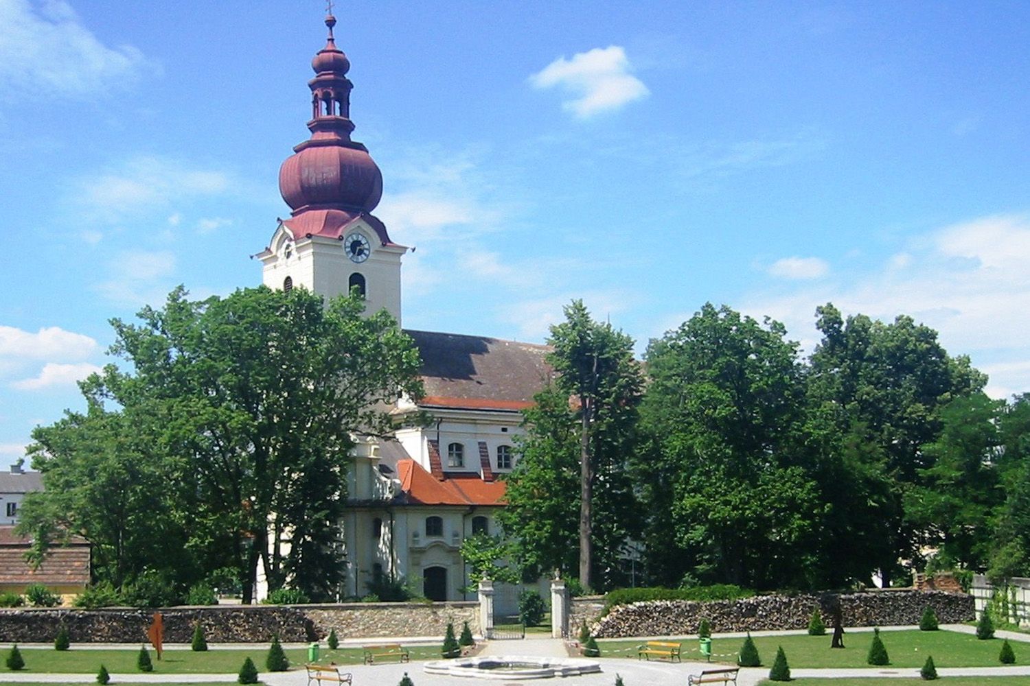 Barockkirche mit rotem Turm und Barockgarten im Vordergrund.