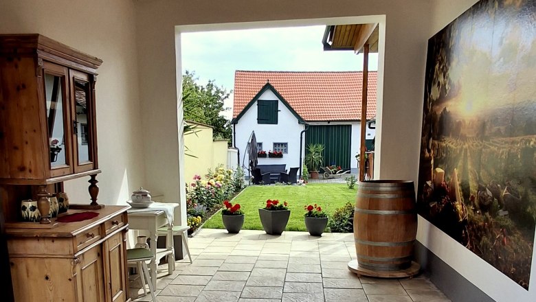 Innenhof mit Holzm&ouml;beln, Pflanzen und Blick auf ein Haus mit rotem Dach.