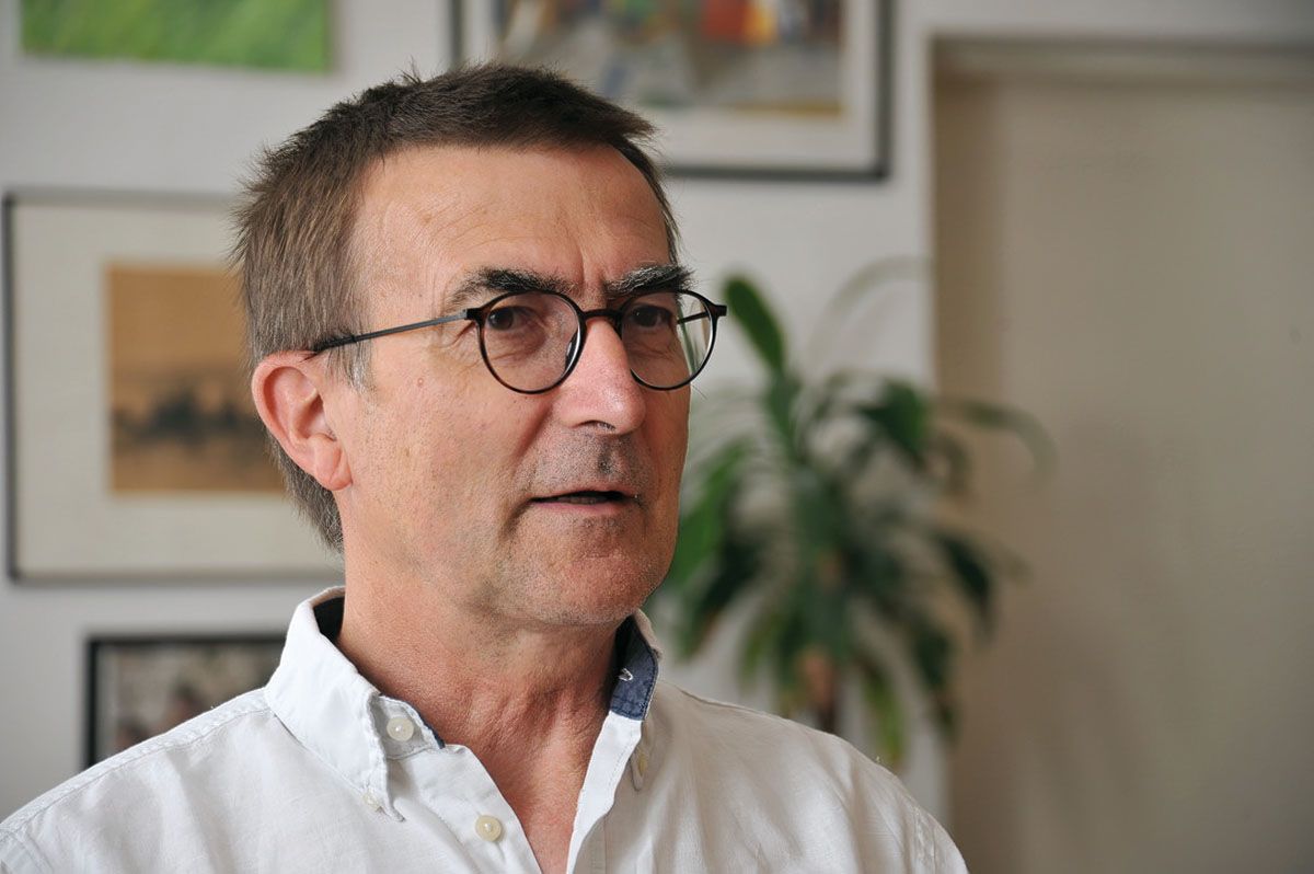 Ein Mann mit Brille und weißem Hemd steht in einem Raum mit Kunstwerken an der Wand.