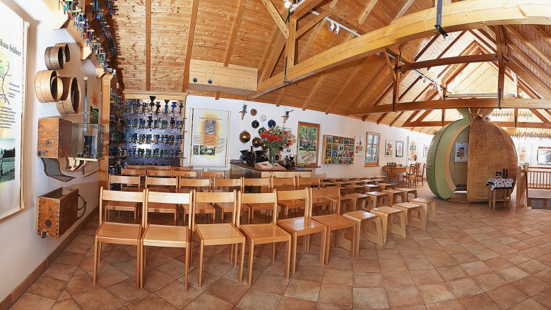 Innenansicht eines Museums mit Holzstühlen, Infotafeln und Ausstellungsstücken an den Wänden.