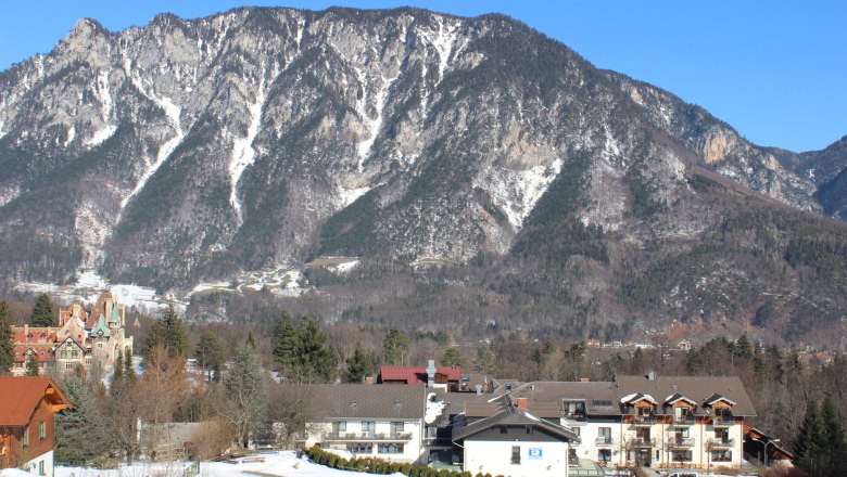 Berglandschaft mit Gebäuden im Vordergrund und schneebedeckten Bergen im Hintergrund.