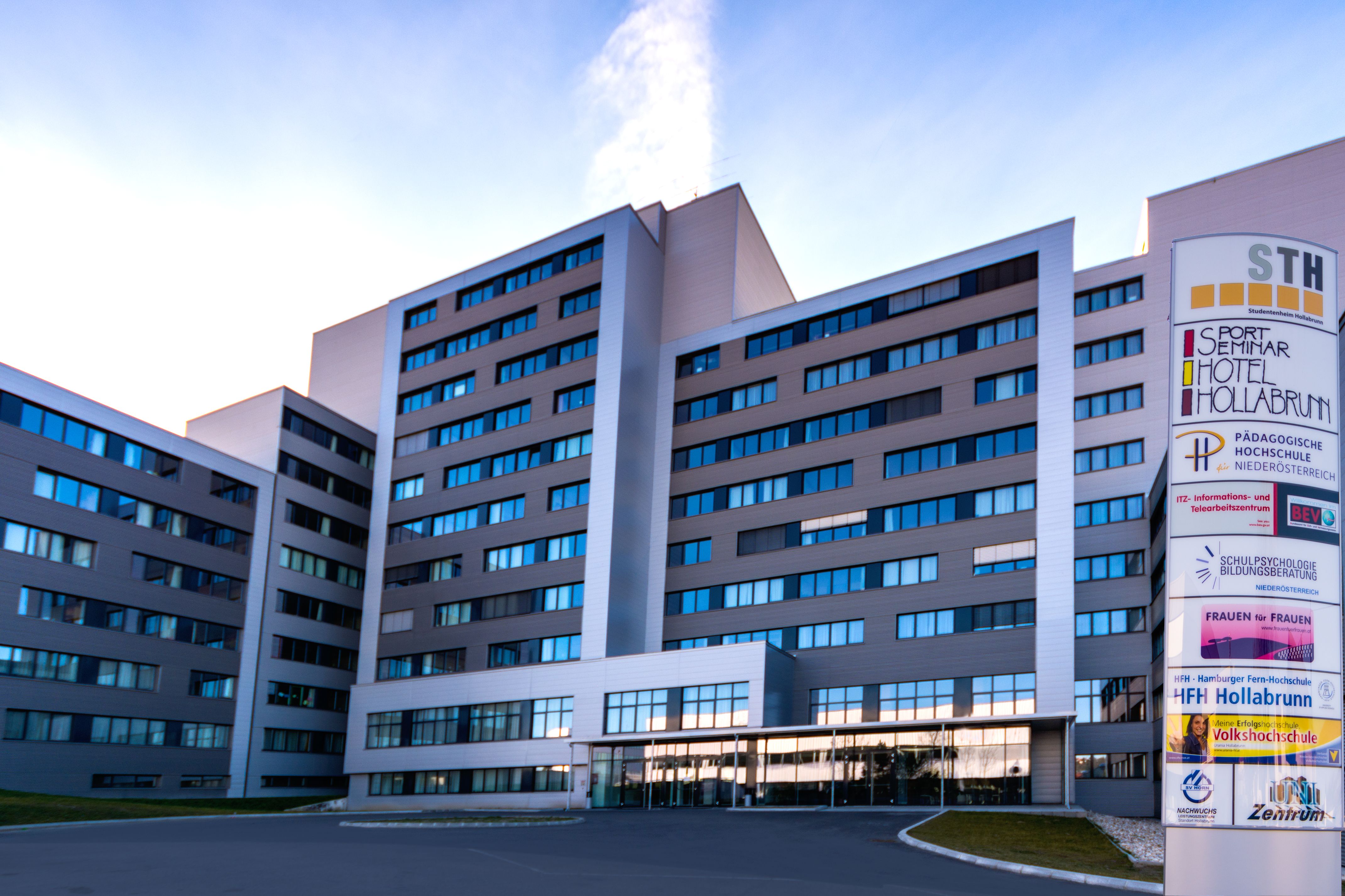 Ein modernes mehrstöckiges Gebäude mit einem Schild, das "Sport Seminar Hotel Hollabrunn" anzeigt.