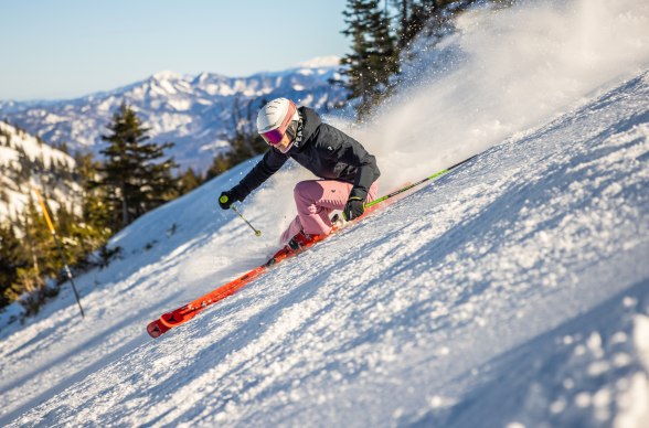 Skifahrer fährt präperierte Skipiste hinunter mit Ausblick auf Berge