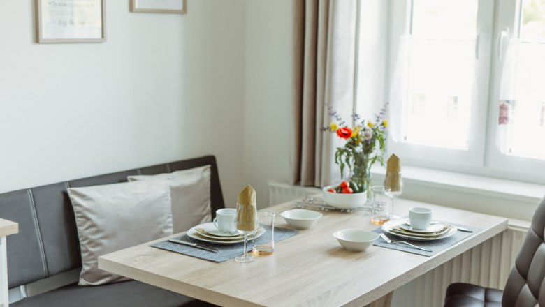 Essbereich in einem modernen Appartement mit gedecktem Tisch und Blumen.