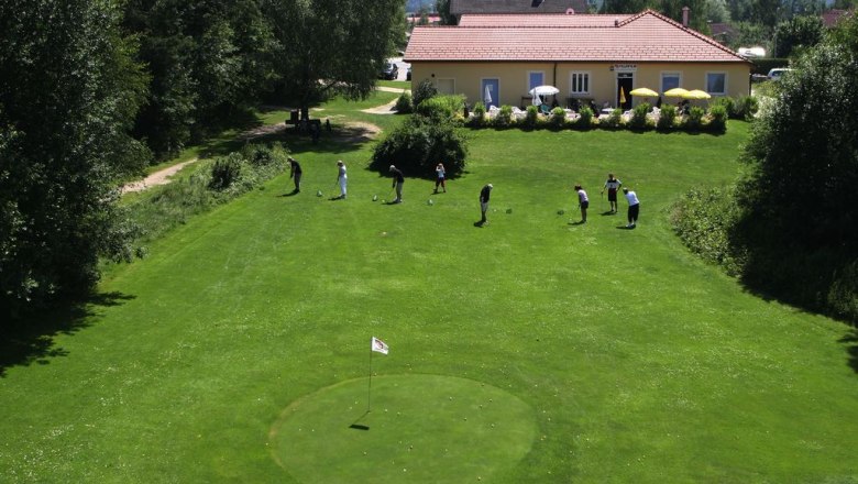 Golfplatz mit Spielern und Clubhaus im Hintergrund.