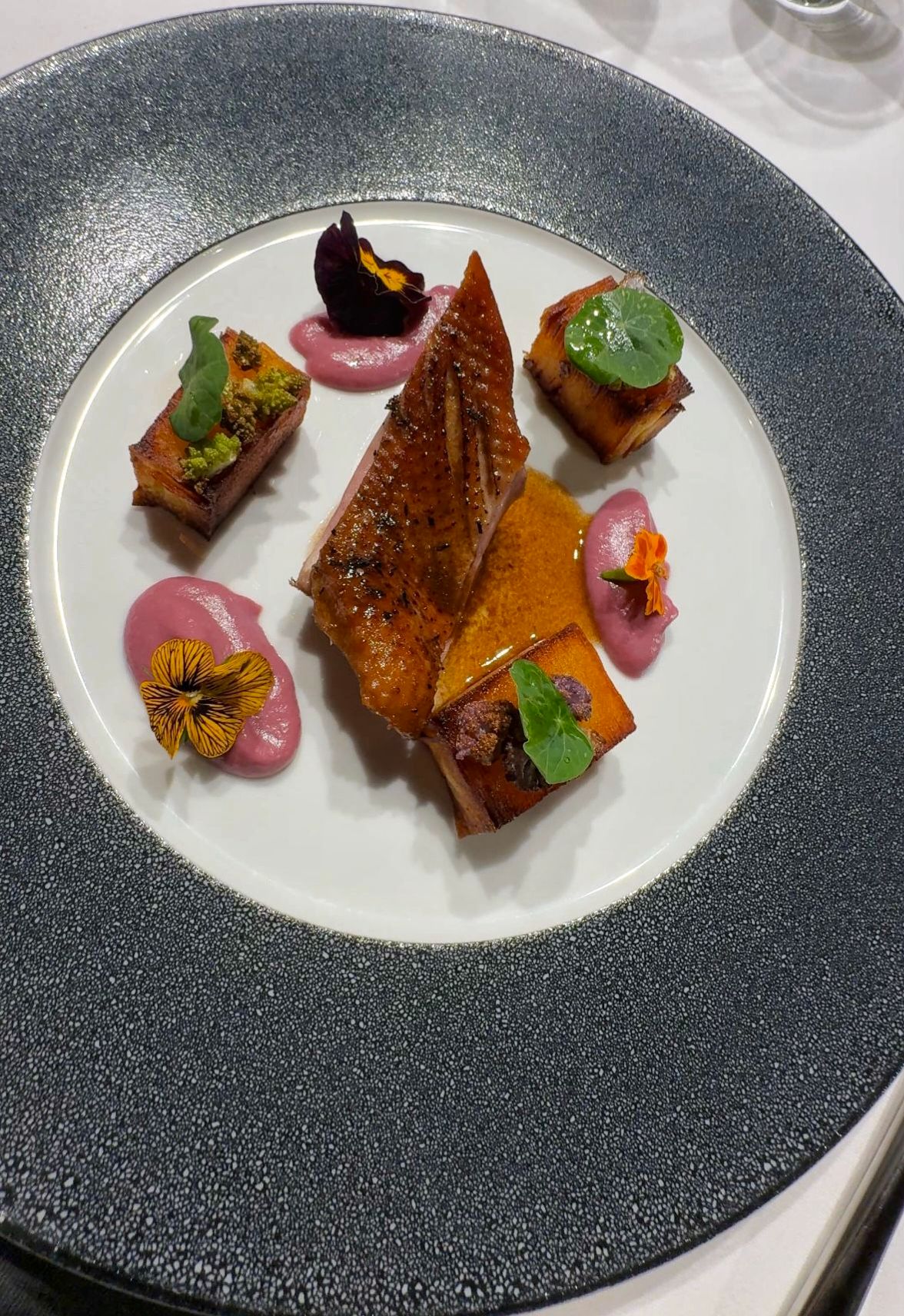 Gourmetgericht mit Entenbrust, Gemüsewürfeln und Blüten auf einem eleganten Teller.