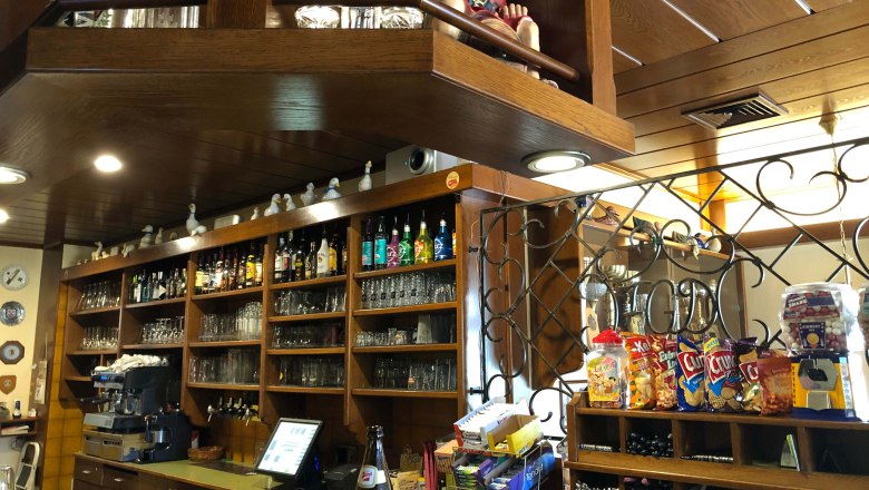 Innenansicht einer Bar mit Holzregalen, Gl&auml;sern, Flaschen und Snacks.