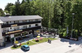 Außenansicht des Gasthofs Berghof mit Terrasse und Parkplatz, umgeben von Bäumen.