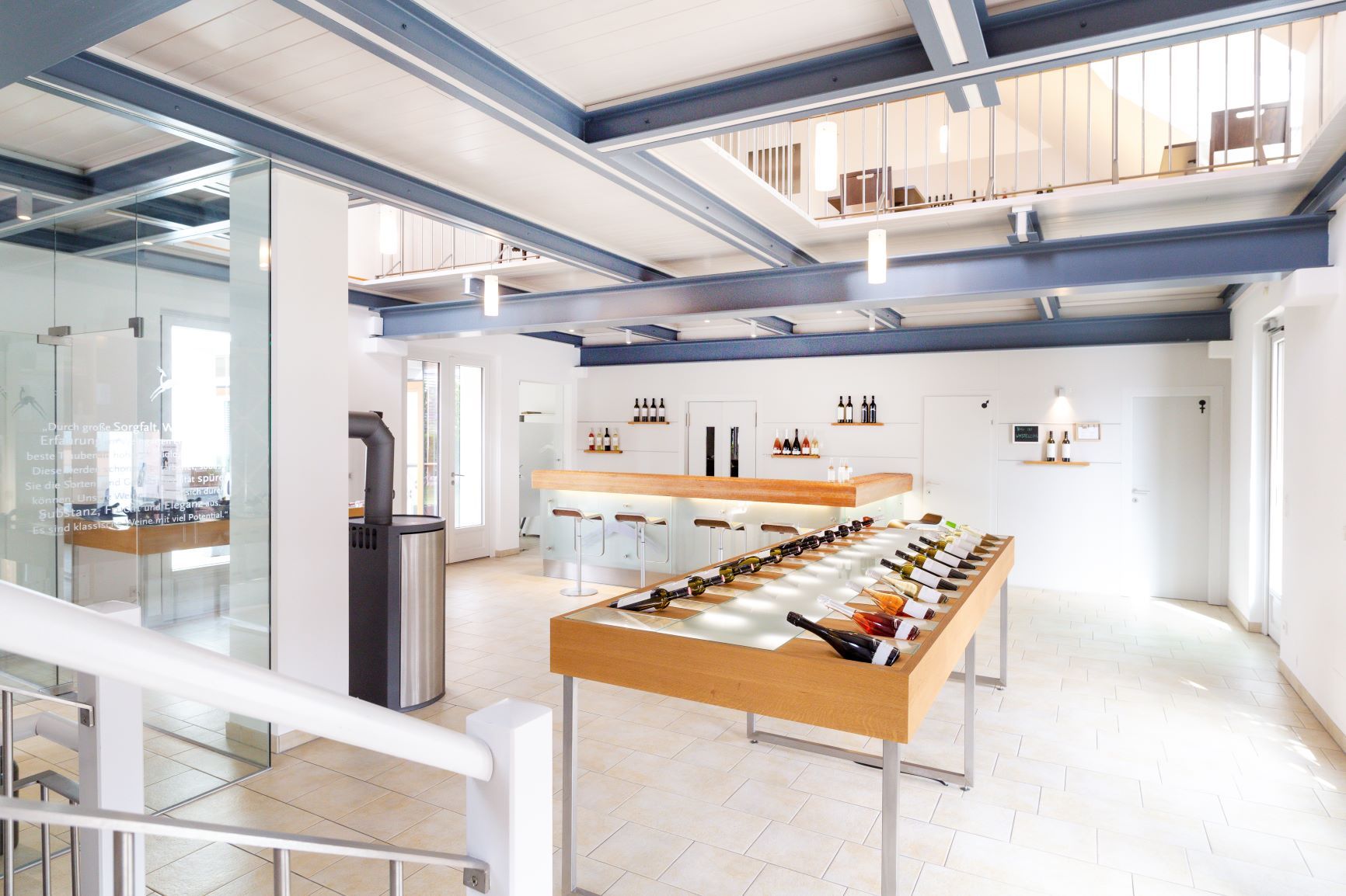 Innenansicht einer modernen Vinothek mit Weinflaschen auf einem Tisch und einer Bar im Hintergrund.